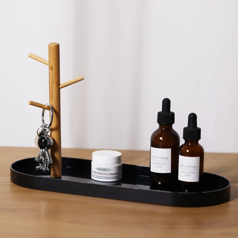 Black jewelry and key tray with wooden tree branch holder, shown with keychain and bottles on a tabletop