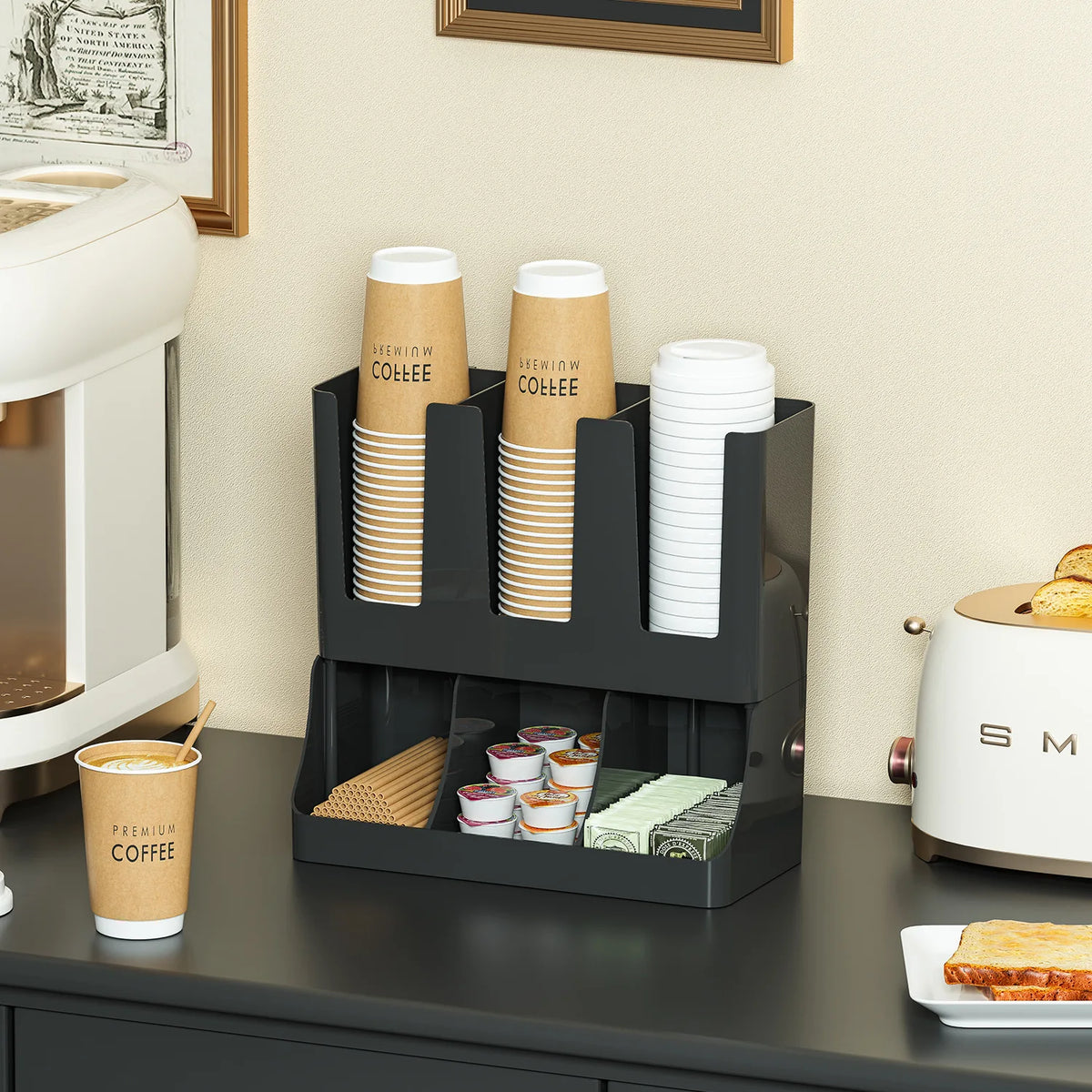 Black plastic coffee station organizer placed on a kitchen counter, compartments filled with coffee cups, pods, stirrers, and condiments.