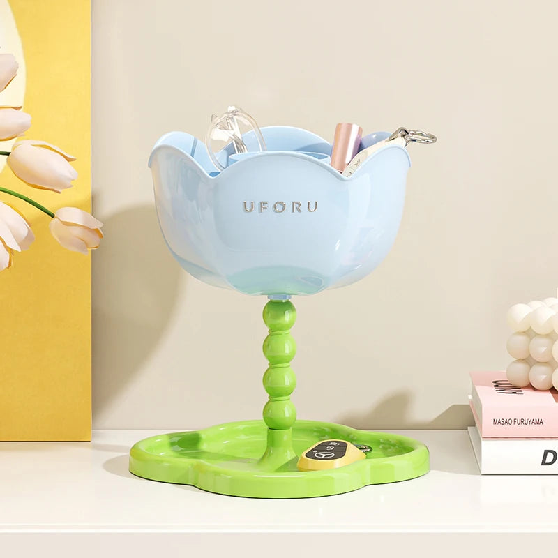 Blue flower-shaped organizer stand with green tray on a white surface, holding glasses and small items