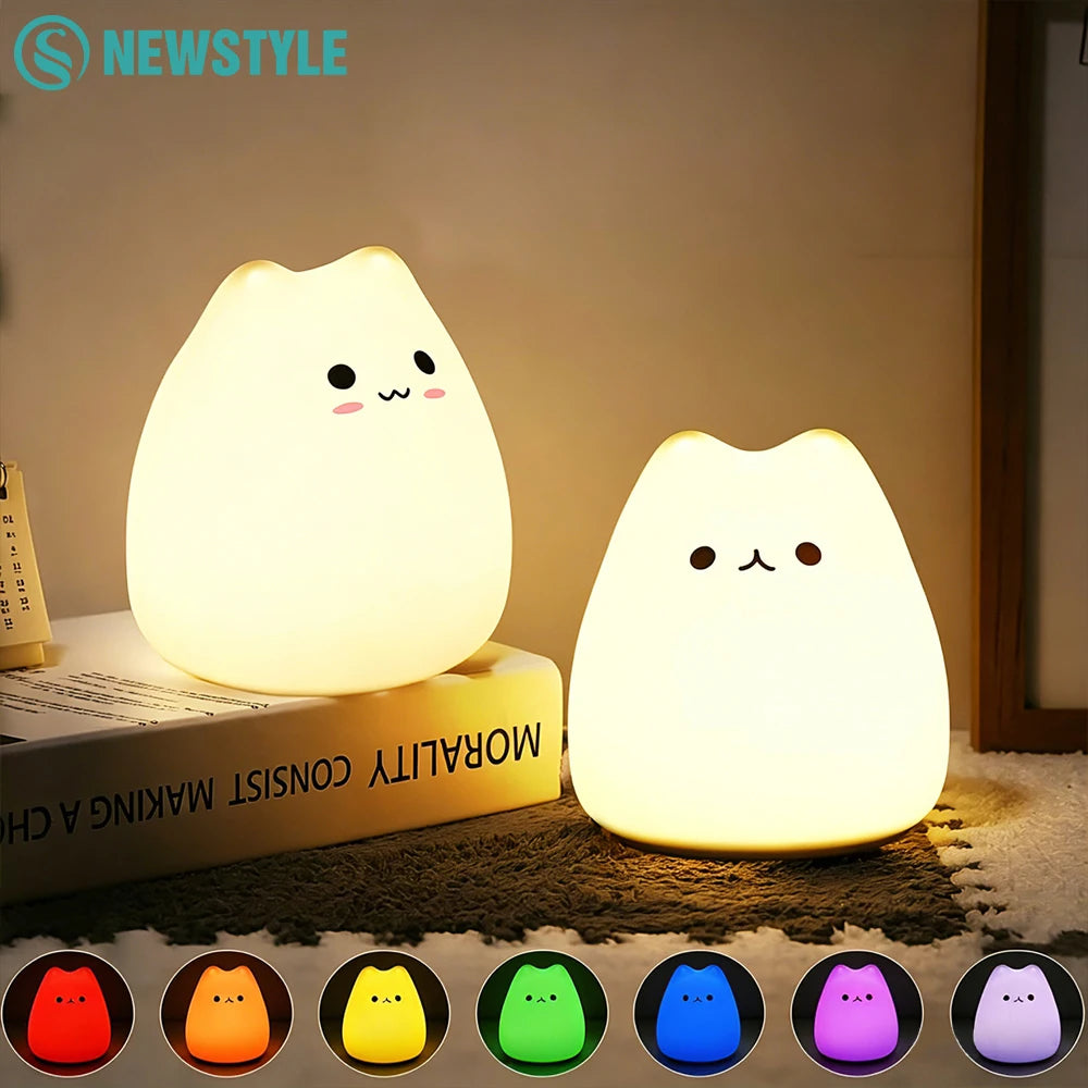 Two silicone cat night lights glowing warmly on a nightstand, with rainbow color options shown below