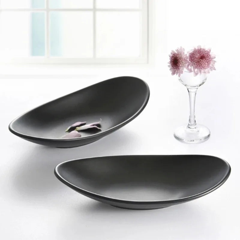 matte black oval ceramic trays styled on a white surface with a glass vase of pink flowers and petals nearby