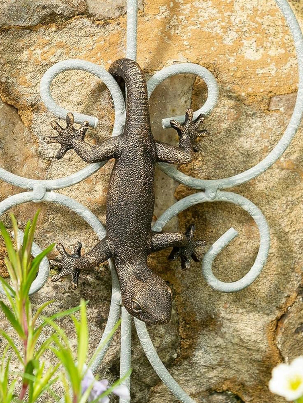 Gecko planter figurine displayed on a metal garden trellis against a stone wall
