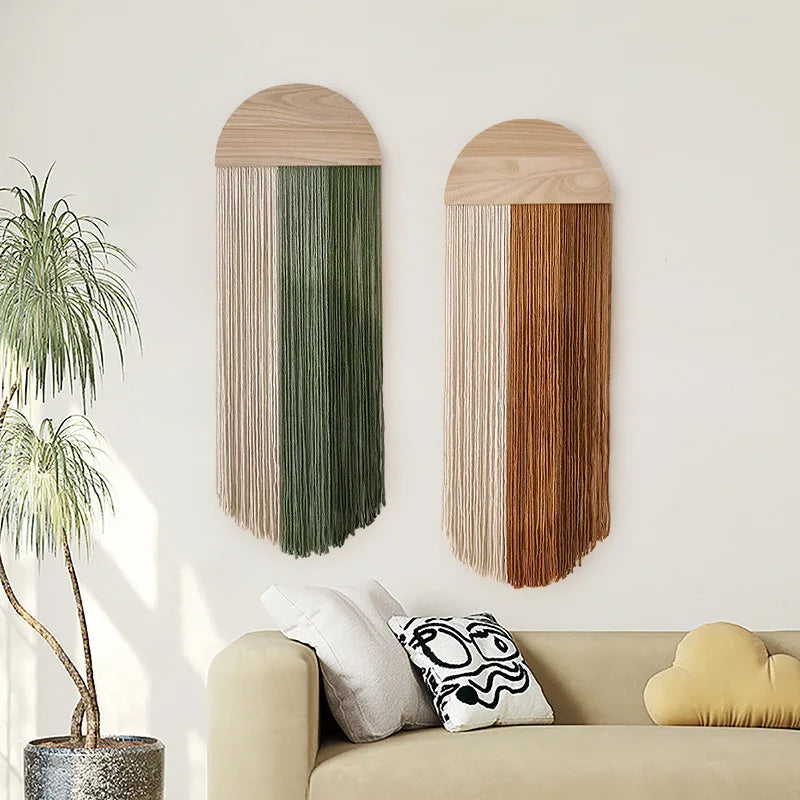 Two woven tassel wall hangings with arched wood tops, one in green and cream, one in brown and cream, hanging above a sofa