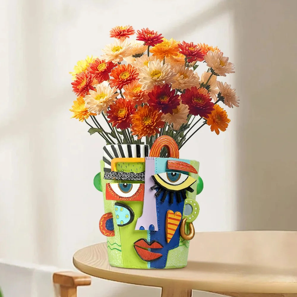 hand-carved face design planter pot holding orange and yellow flowers on a table