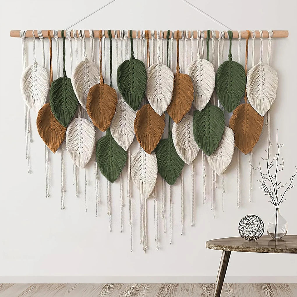 leaf macrame wall hanging in neutral and green tones on a white wall above a table