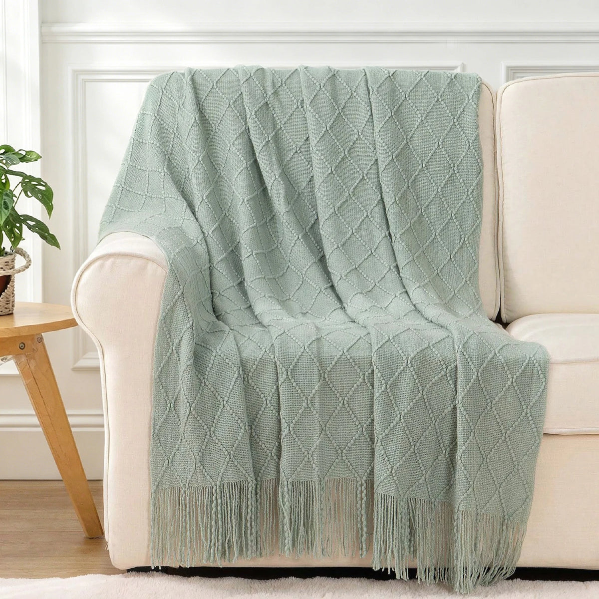Plaid knit throw blanket in sage green draped over a cream sofa with fringe tassels