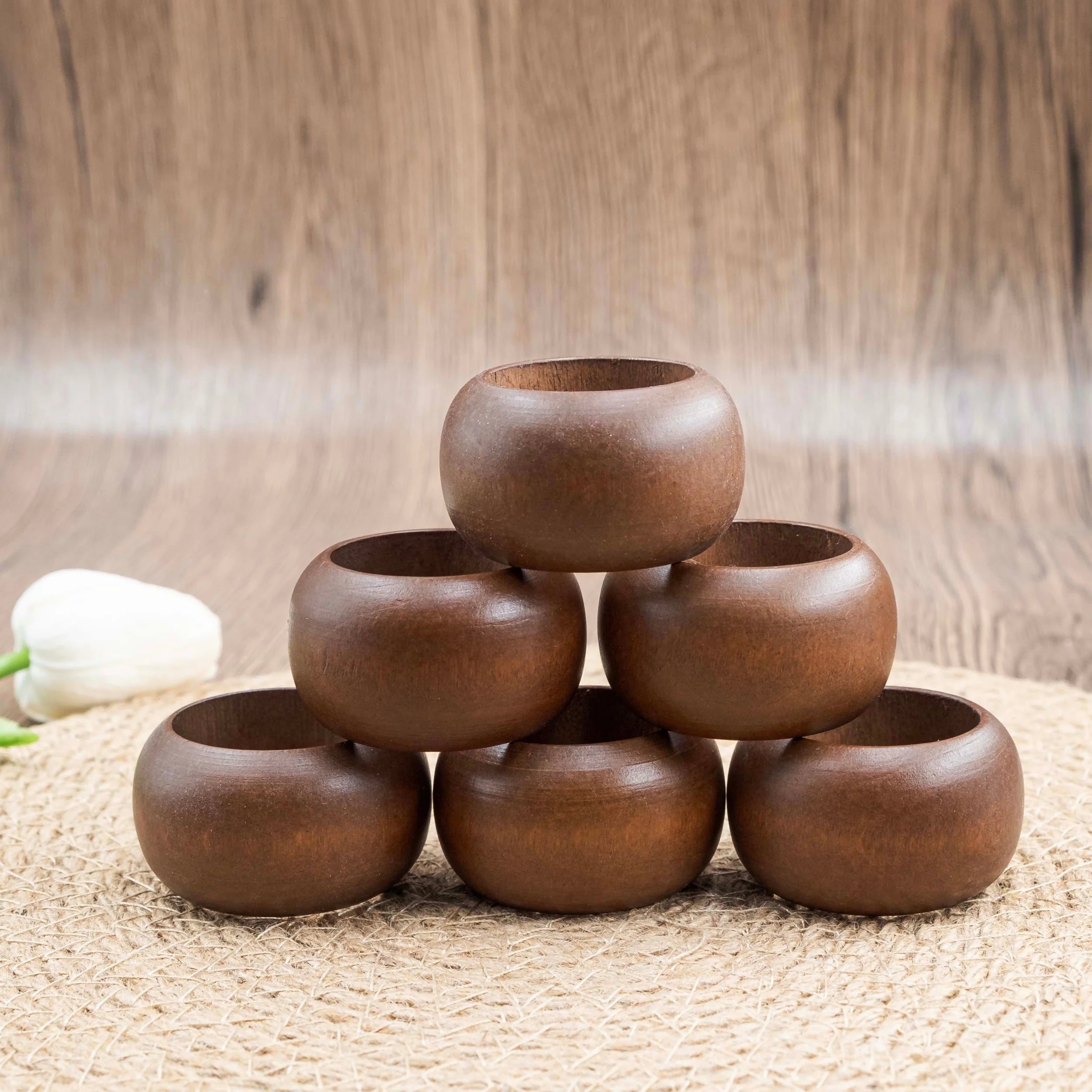 Stack of six round acacia wood napkin rings on a woven placemat with neutral wood background