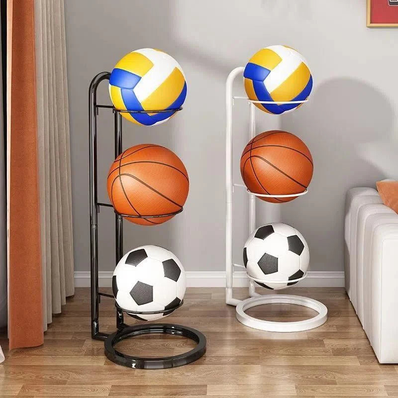 Black and white freestanding ball storage racks holding basketballs, volleyballs, and soccer balls in a cozy living room with wooden floors.