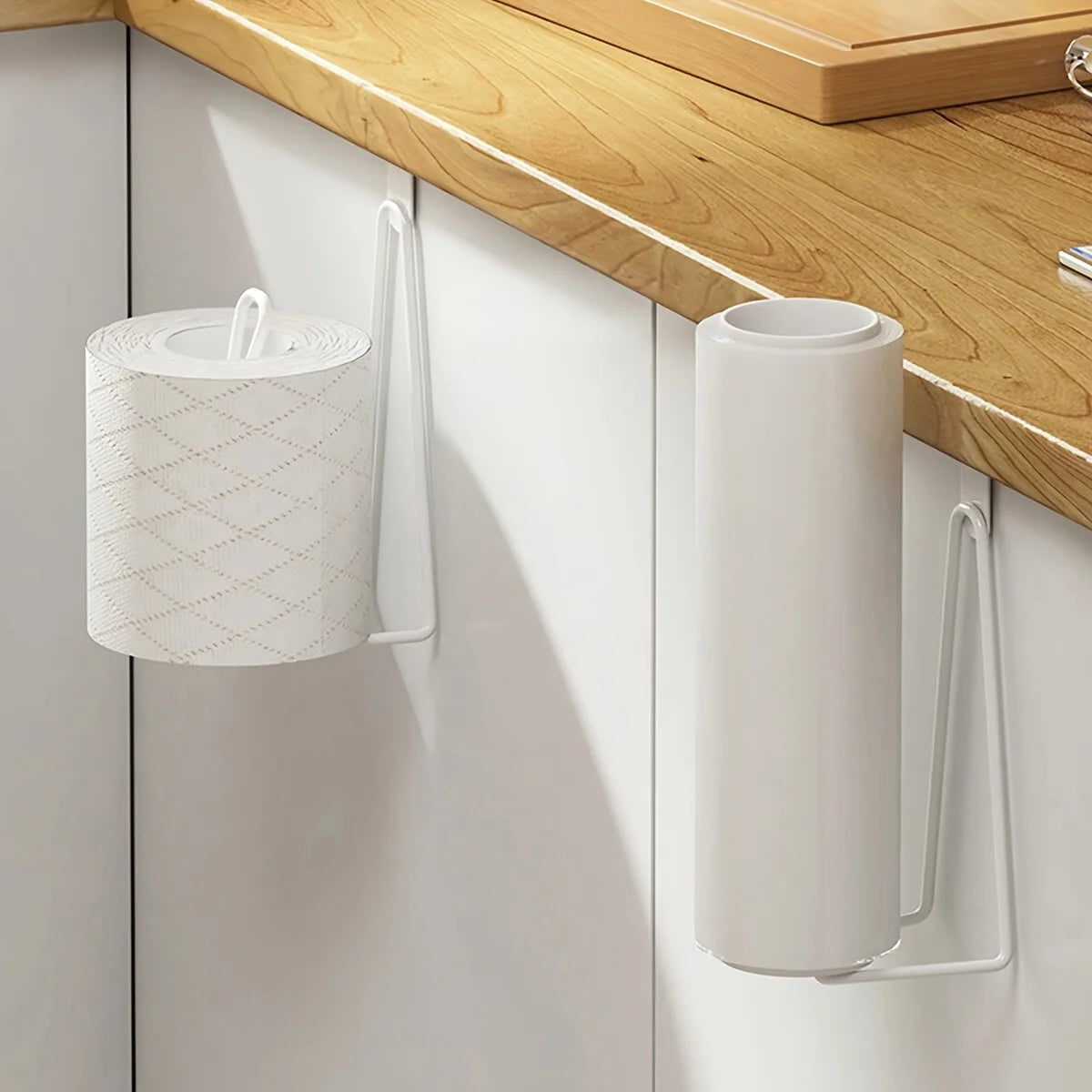 white metal over cabinet holder on a kitchen cabinet holding a paper towel roll and a toilet paper roll