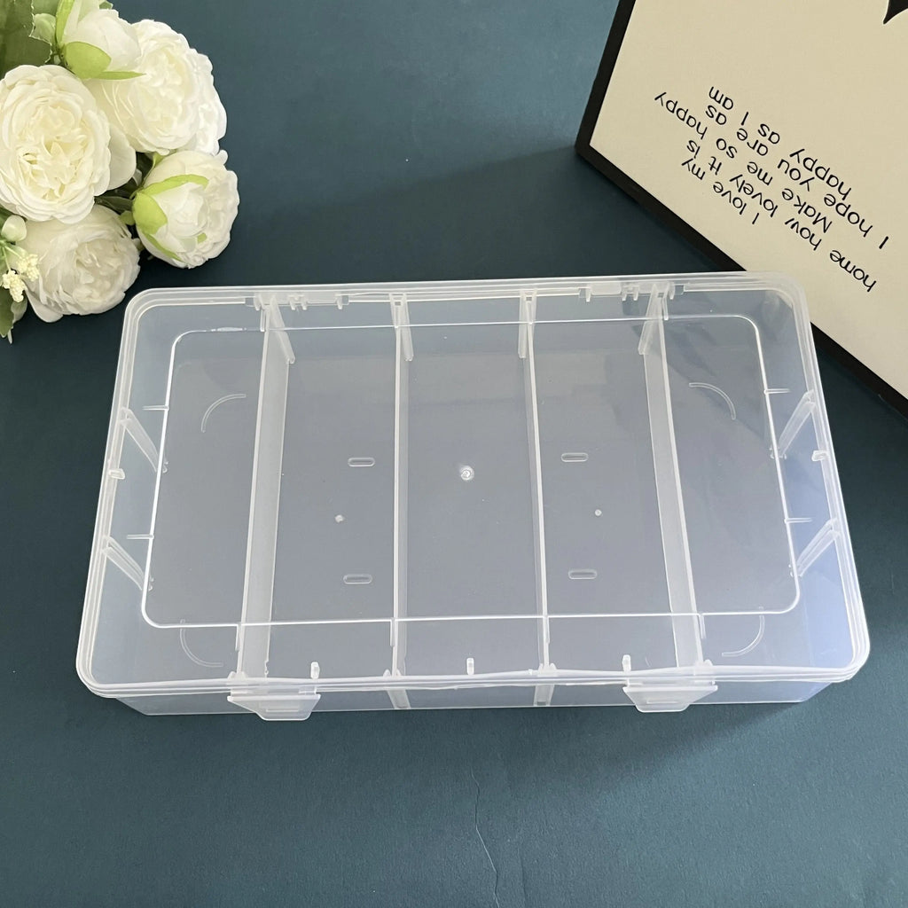 Closed clear plastic organizer box with 5 compartments, on a blue tabletop