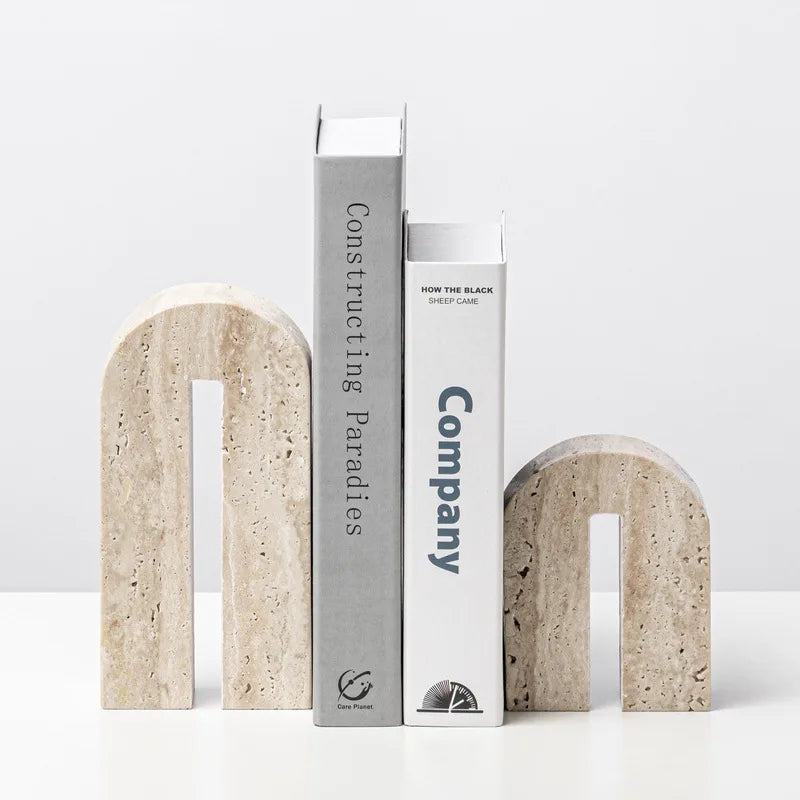 Two arched travertine stone bookends in beige holding books upright on a modern white shelf