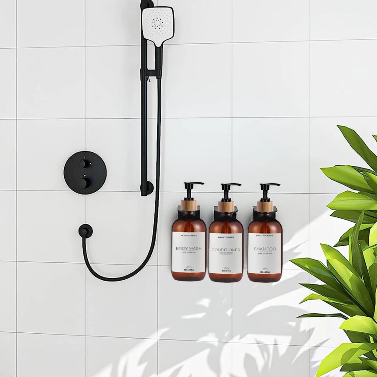 Shampoo, conditioner, and body wash amber dispenser bottles on a white tiled shower wall with greenery in the foreground