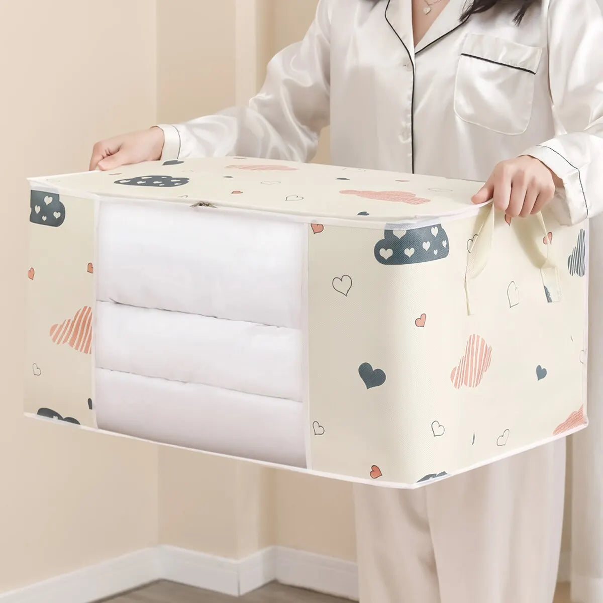Person lifting a beige large foldable storage bag filled with bedding, showing reinforced soft handles.