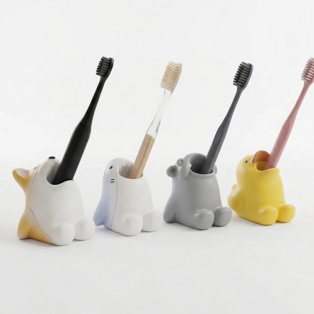 Group of four animal toothbrush holders on a plain surface, each holding a toothbrush—Corgi, Shark, Hippo, and Duckling styles.