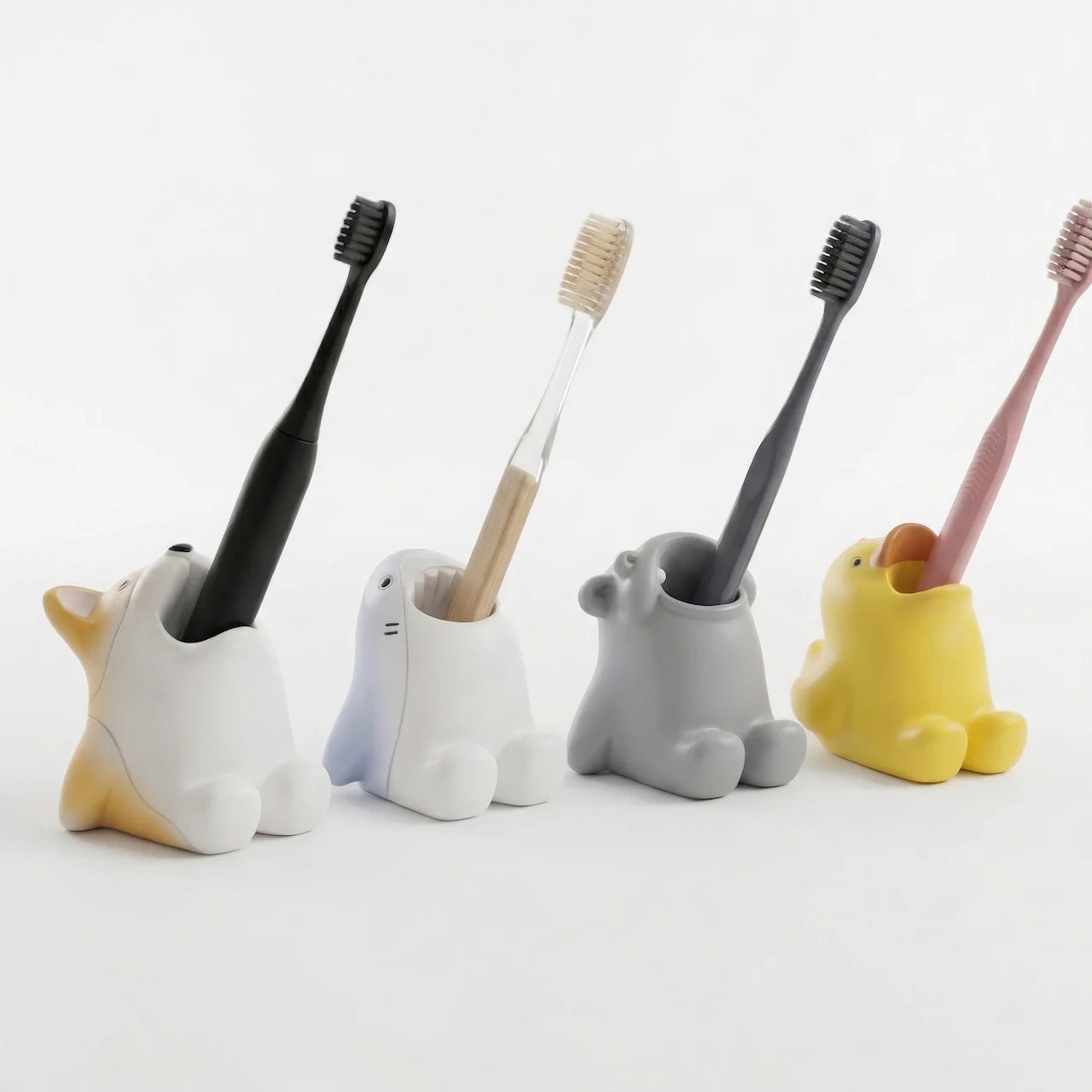 Group of four animal toothbrush holders on a plain surface, each holding a toothbrush—Corgi, Shark, Hippo, and Duckling styles.