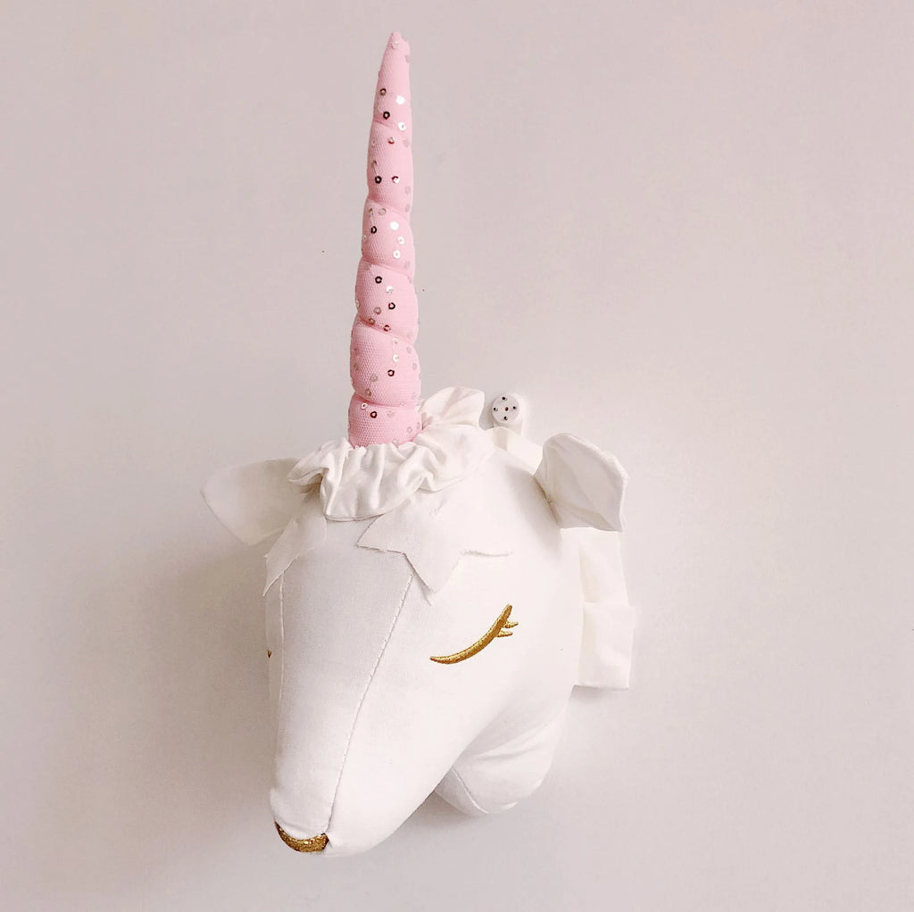 Close-up of a plush unicorn animal head wall hanging, white with pink horn and sequin details