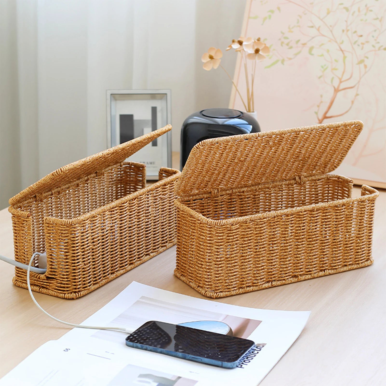 Two hand-woven style cable organizer boxes on a tabletop in a cozy room
