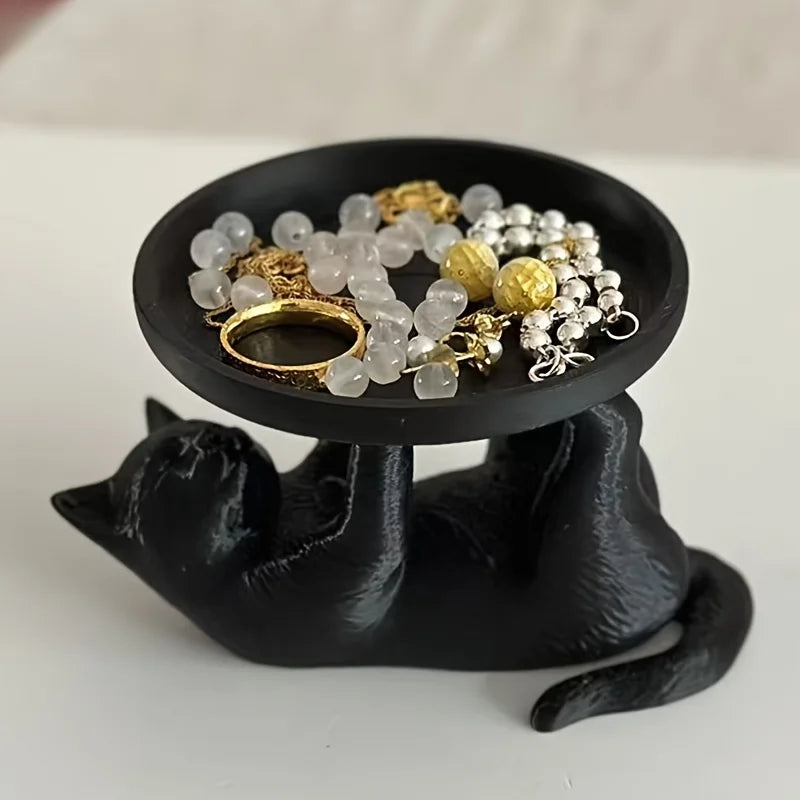 Black cat catchall tray holding gold and pearl jewelry on a white surface