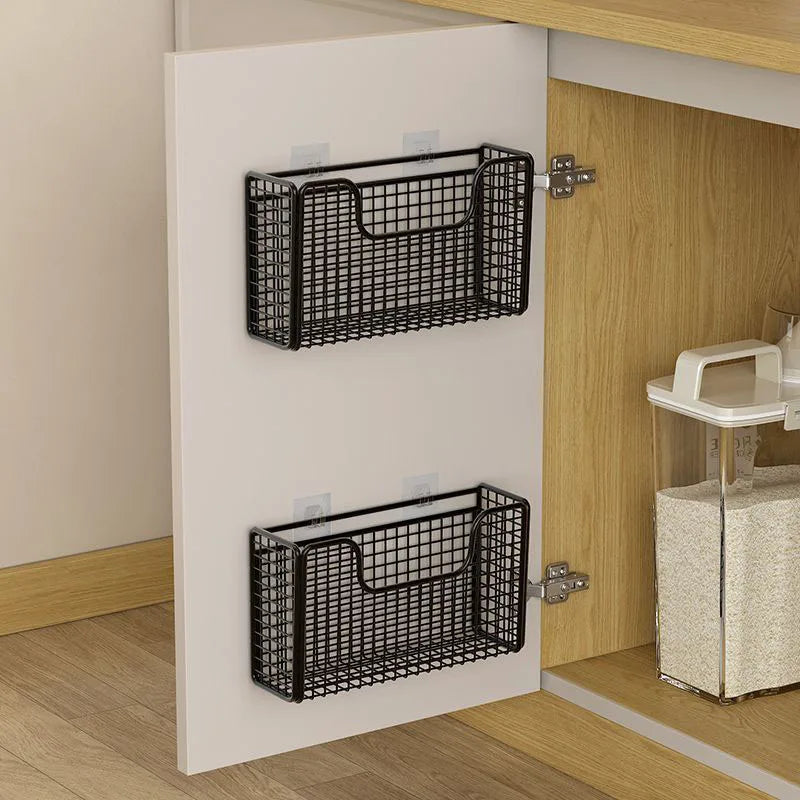 Two black iron storage baskets mounted on the inside of a kitchen cabinet door for organizing supplies