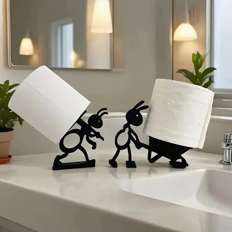 Two ant-shaped black tissue holders on a bathroom vanity, each supporting a single paper roll amidst plants and a mirror.
