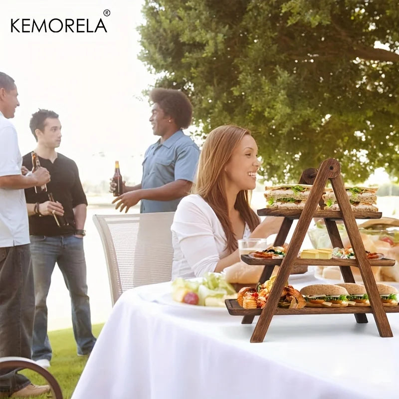 people at an outdoor gathering with sandwiches and snacks displayed on a wooden 3-tier serving stand