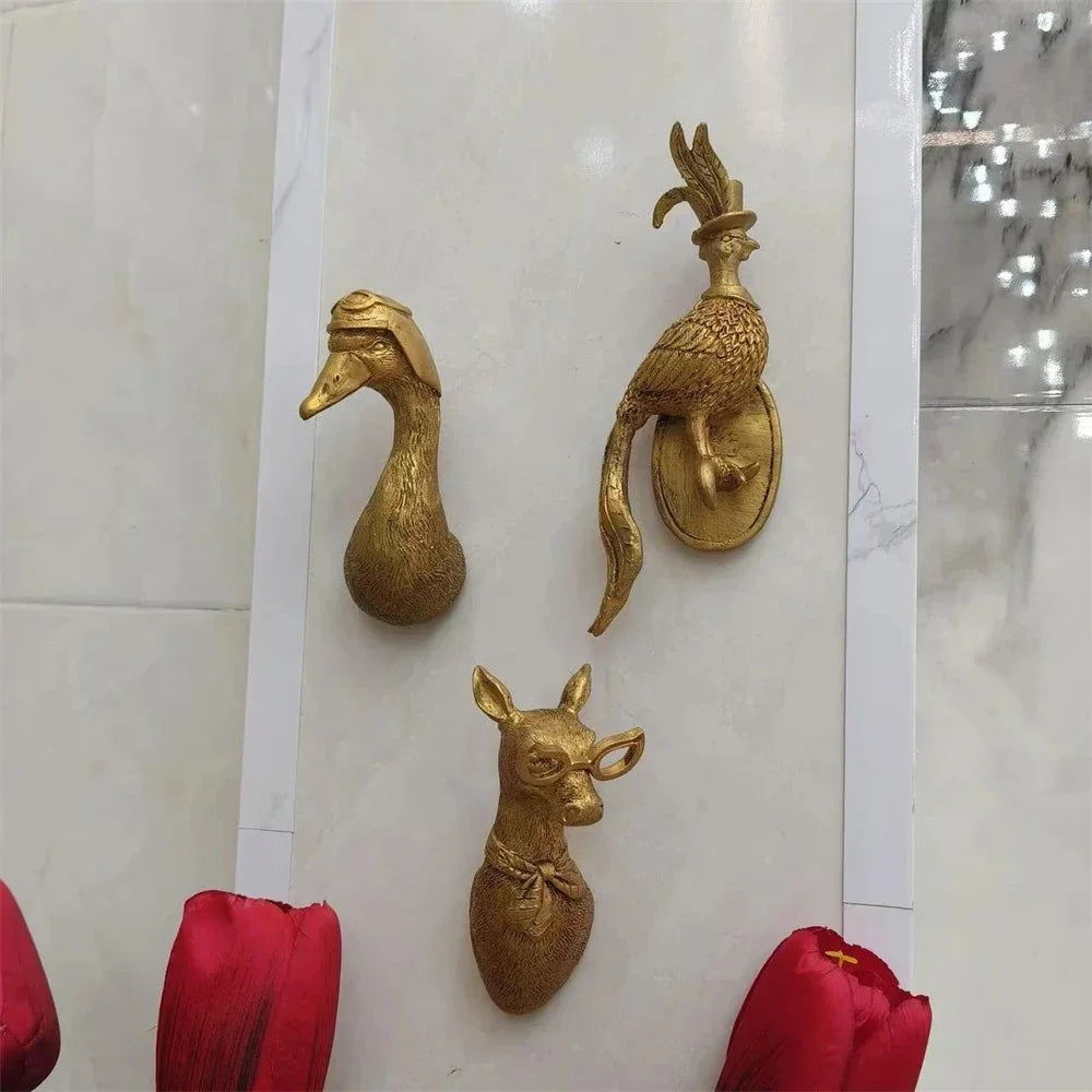set of three gold animal wall hooks on a tiled wall with red flowers below