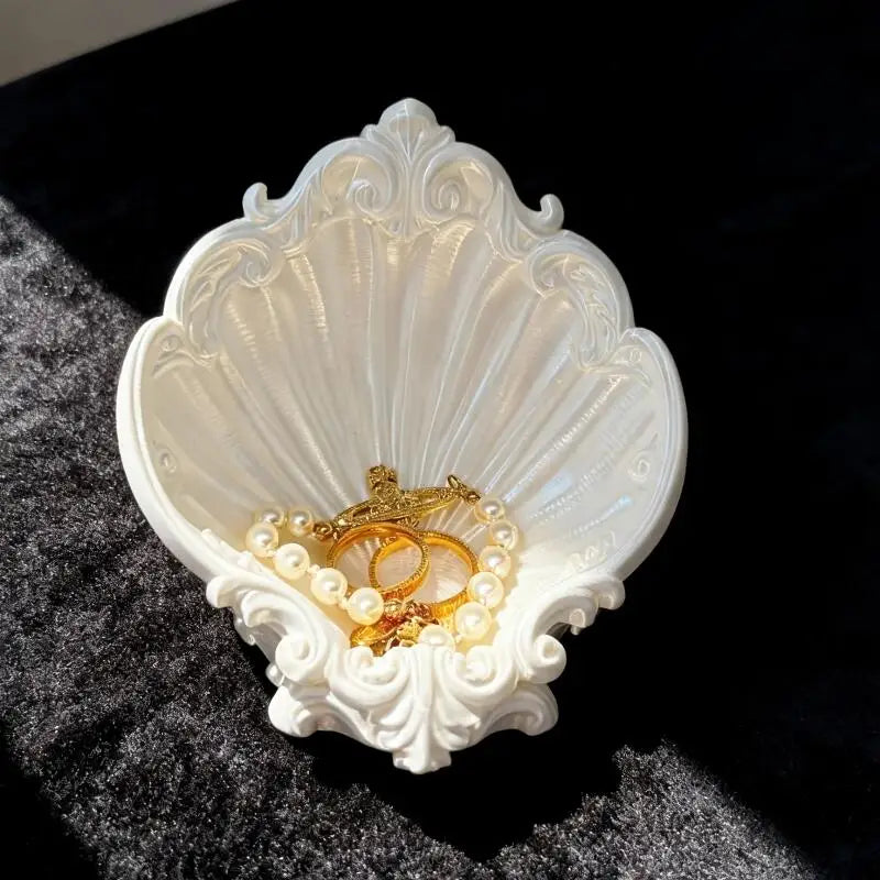 Ornate shell trinket tray with rings and pearl bracelet on a black background