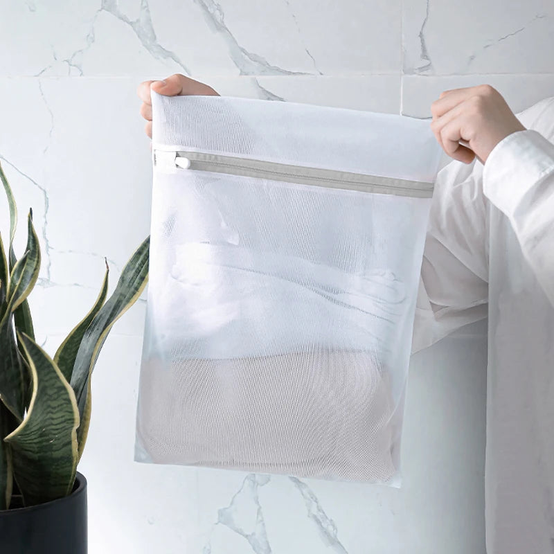 Person holding a medium mesh laundry bag with zipper, partially filled with clothing