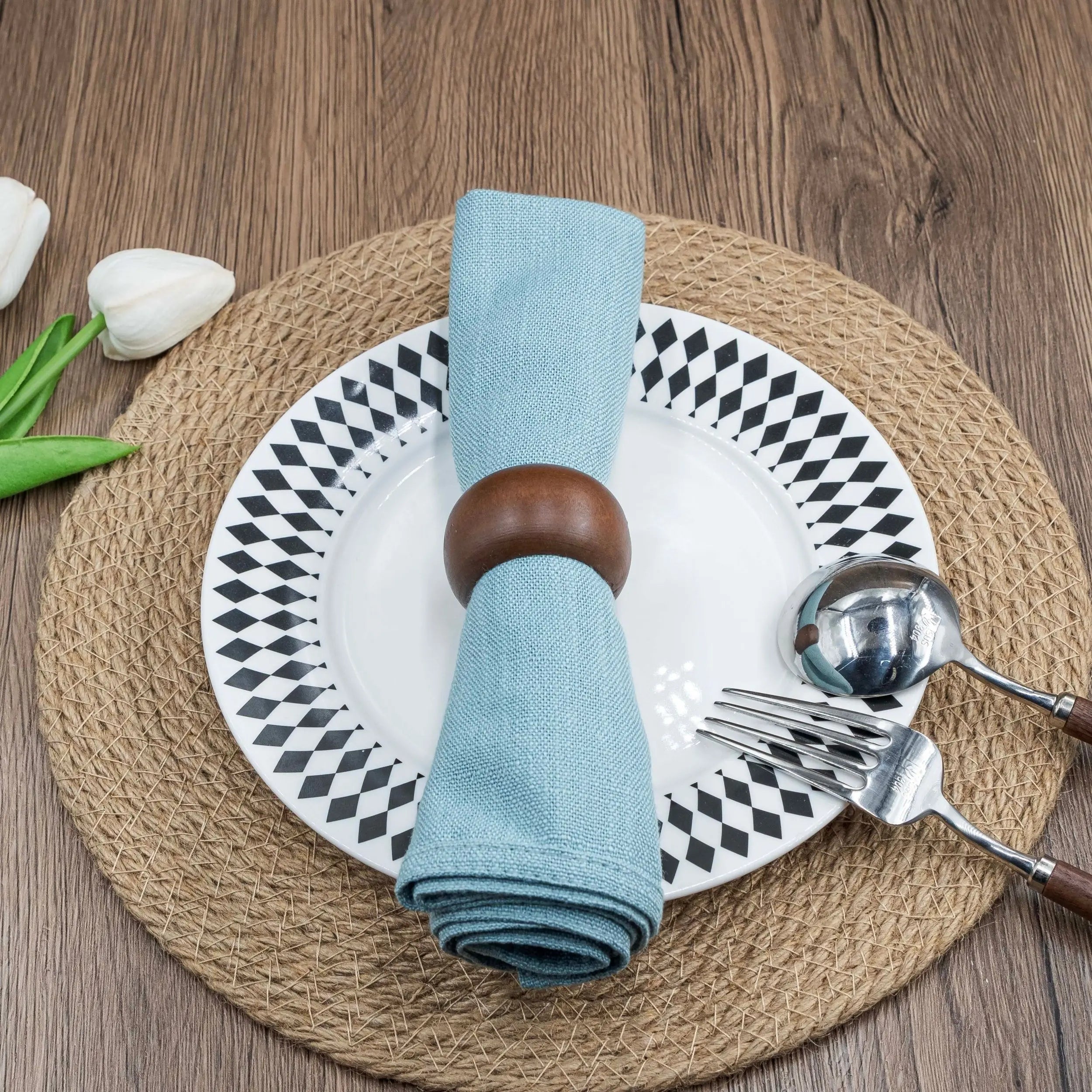 Dining table place setting with blue napkin in acacia wood ring, set on a patterned plate