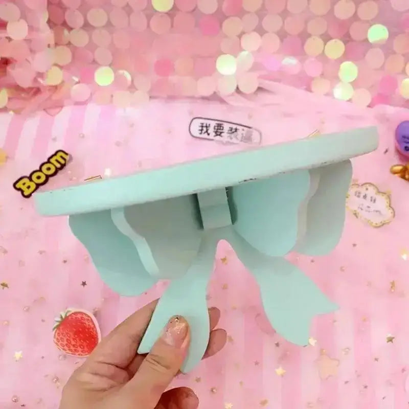 Hand holding a mint green bow-shaped wooden wall shelf against a pink background