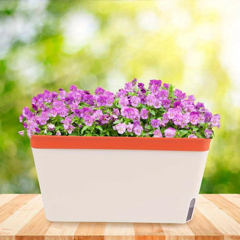 White and orange self-watering planter with purple flowers on a wooden table in natural light