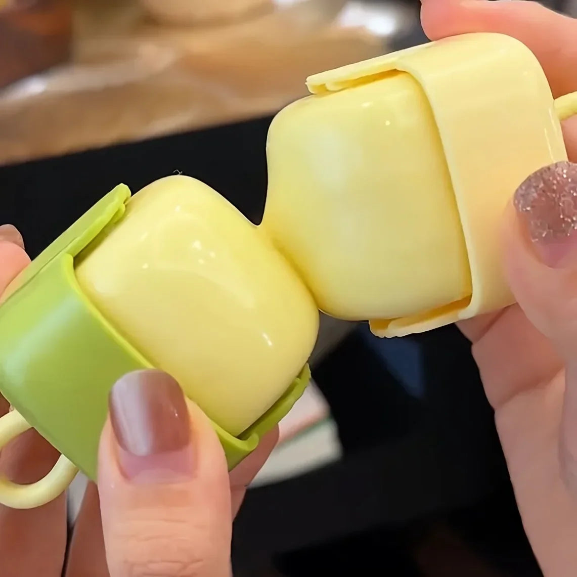 Two hands holding a portable washable lint roller in yellow and green, showing the roller halves connecting