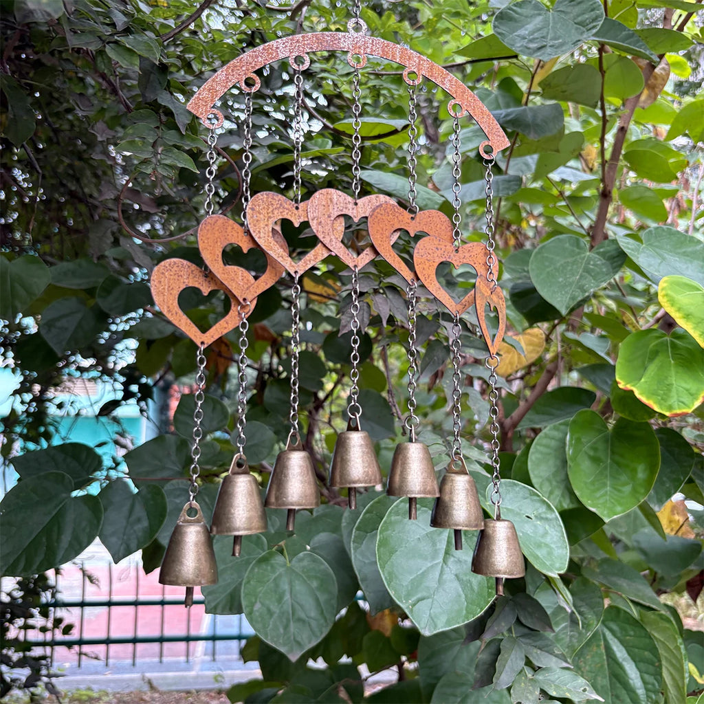 Heart-shaped metal wind chime with bells hanging among green leaves outdoors