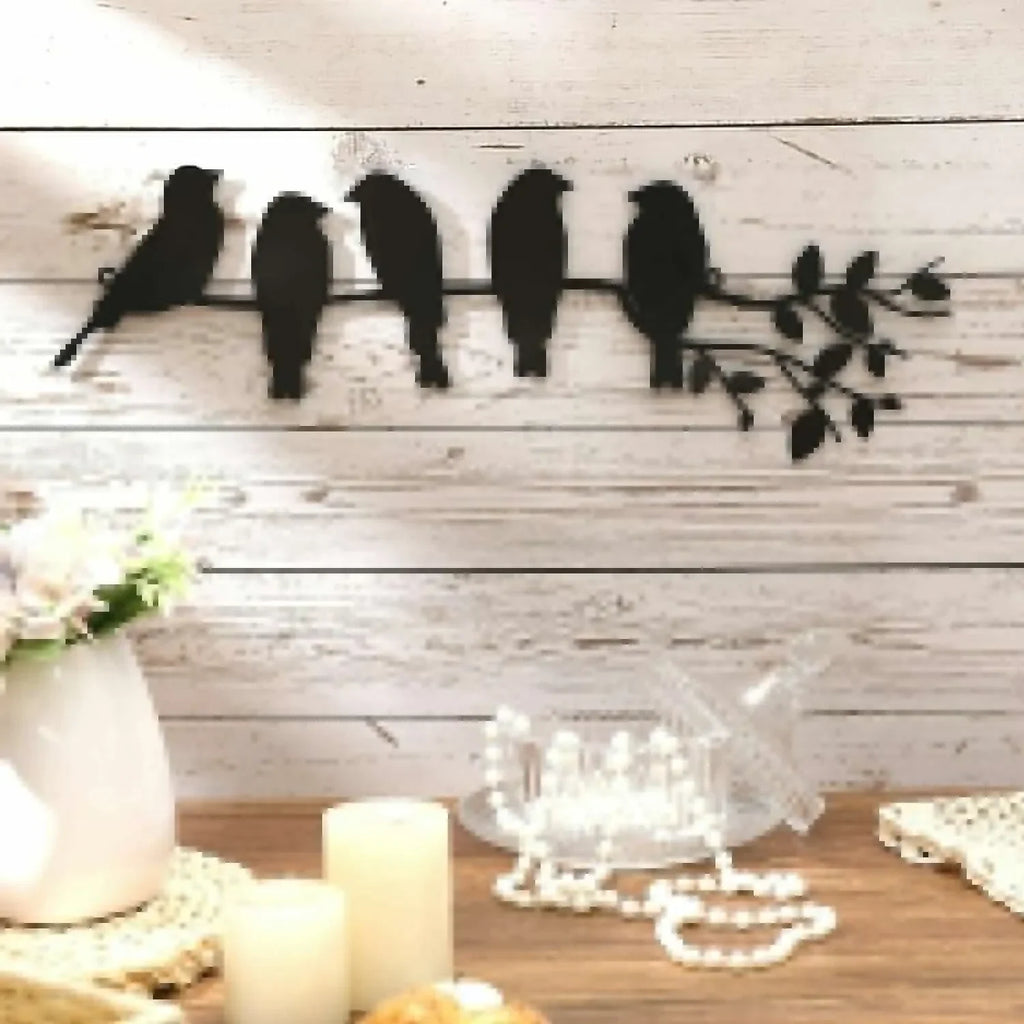 Metal bird wall art with five birds on a branch, displayed on a white wood wall above a cozy home table.