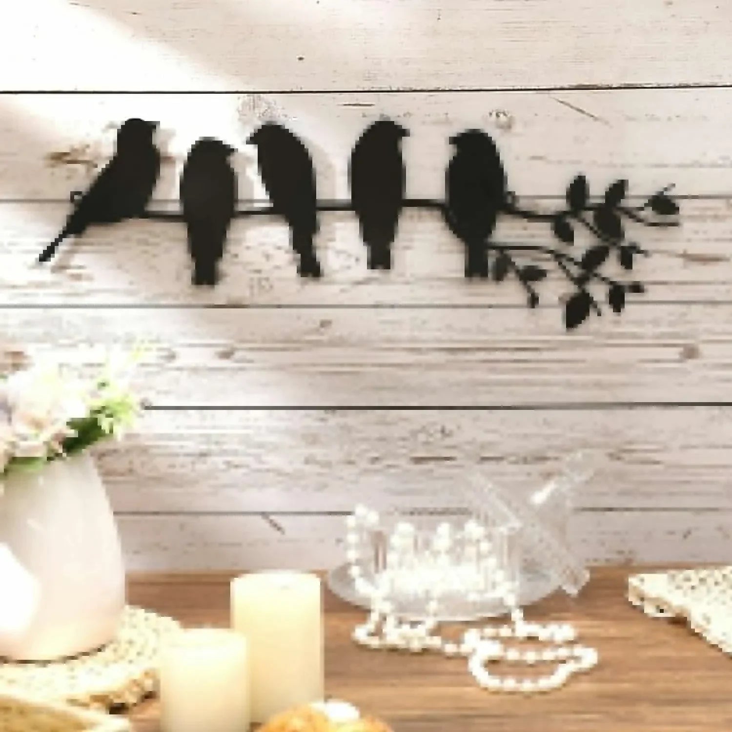 Metal bird wall art with five birds on a branch, displayed on a white wood wall above a cozy home table.