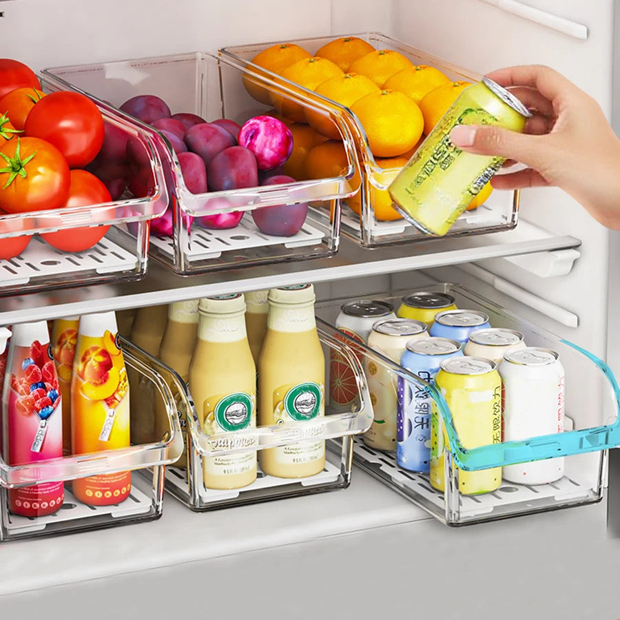 Clear refrigerator organizer bins holding tomatoes, plums, oranges, drinks, and a hand retrieving a can.