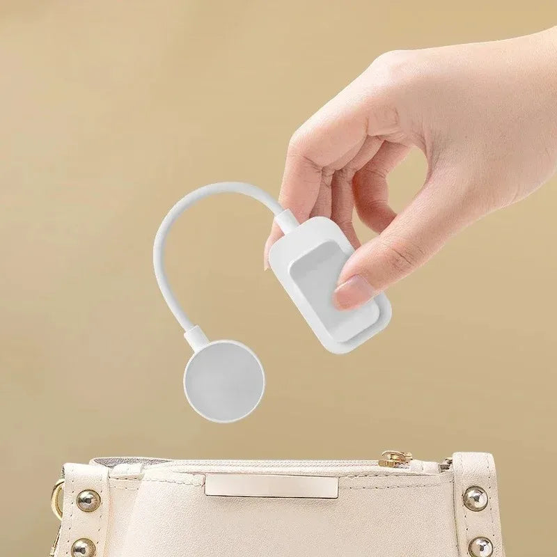 Hand placing mini white clip-on book light into a cream colored handbag, showing size and portability