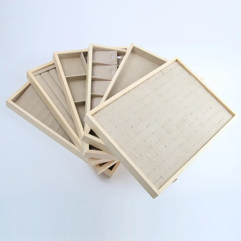 Assorted beige and apricot velvet jewelry trays with wood frames in different compartment styles, fanned out on a light background
