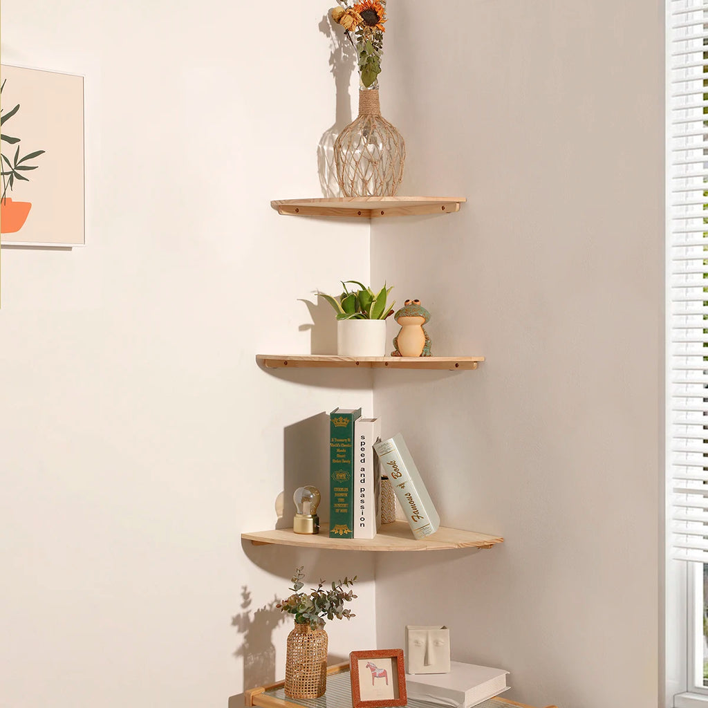 Three-tier solid pine wood floating corner shelves styled in a living room corner, holding books, a plant, and decorative objects