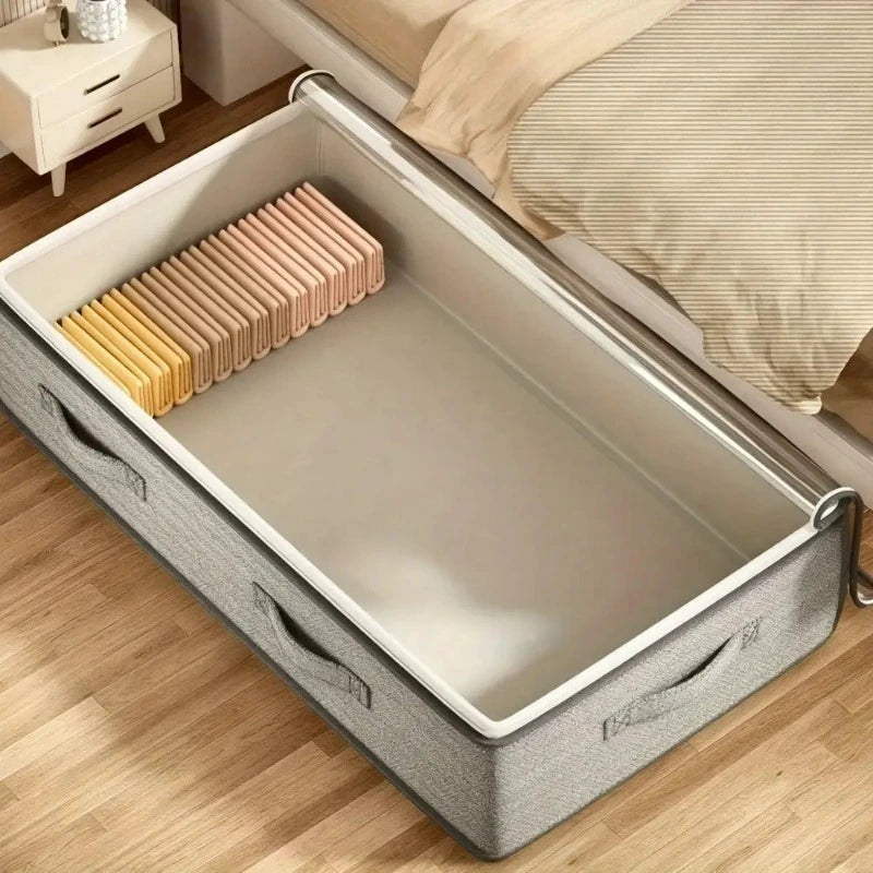 Gray fabric under-bed storage bin with handles and zipper lid, open next to a bed with hangers inside