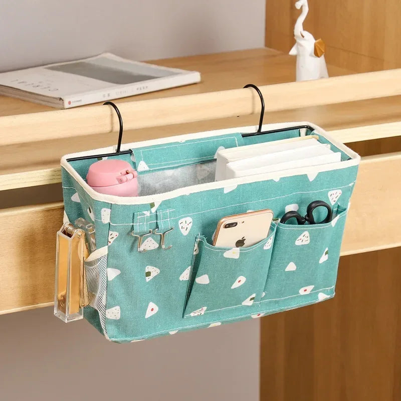 Teal heart-print hanging bedside caddy hooked on a wooden desk, holding notebooks, phone, and accessories