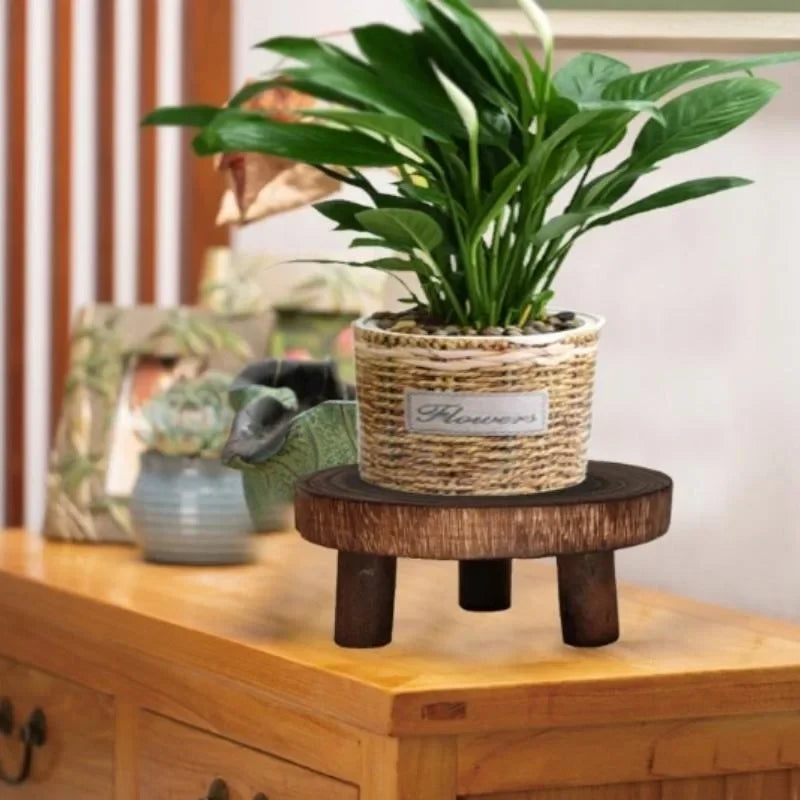 A side view of a dark wood plant stand on a wooden table with a potted plant.