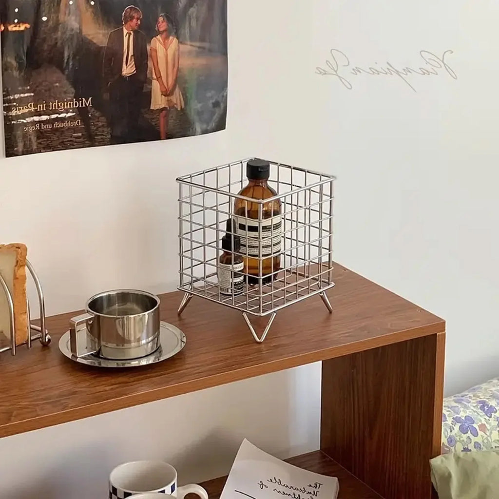silver metal storage basket with bottles on a wooden shelf in a bedroom