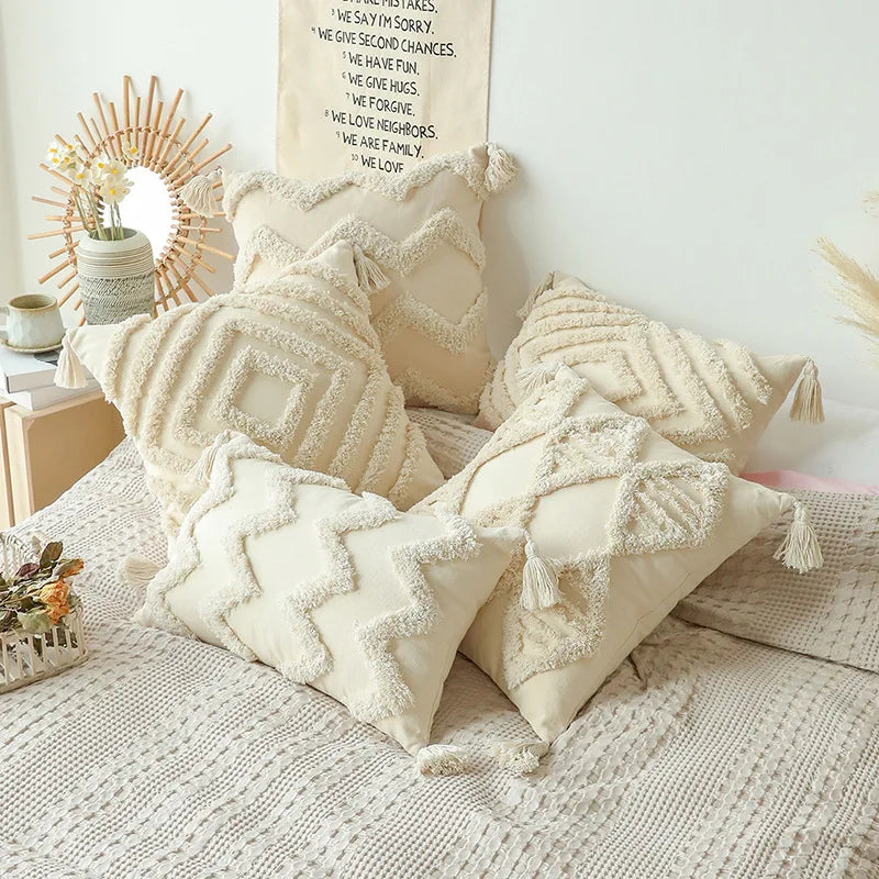Assorted tufted cotton pillow covers with tassels styled on a bed in a cozy bedroom setting