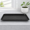 Rectangular black plastic boot tray on a light gray surface in entryway setting