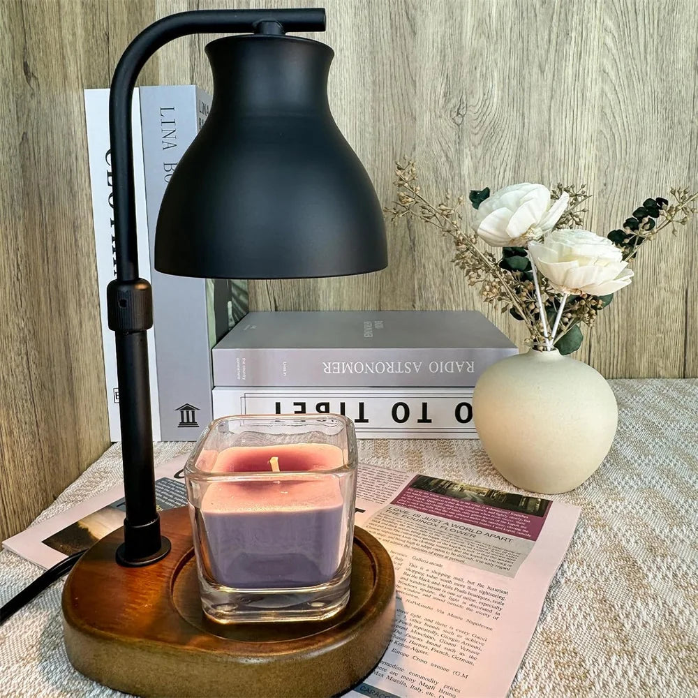 Candle warming lamp on a desk with a square purple candle and a vase of white flowers
