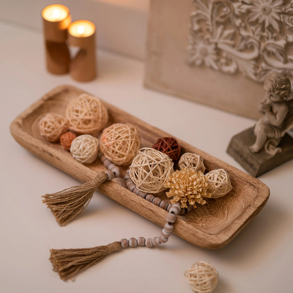 Wood tray styled with rattan balls, beaded tassel, and candles on a white tabletop