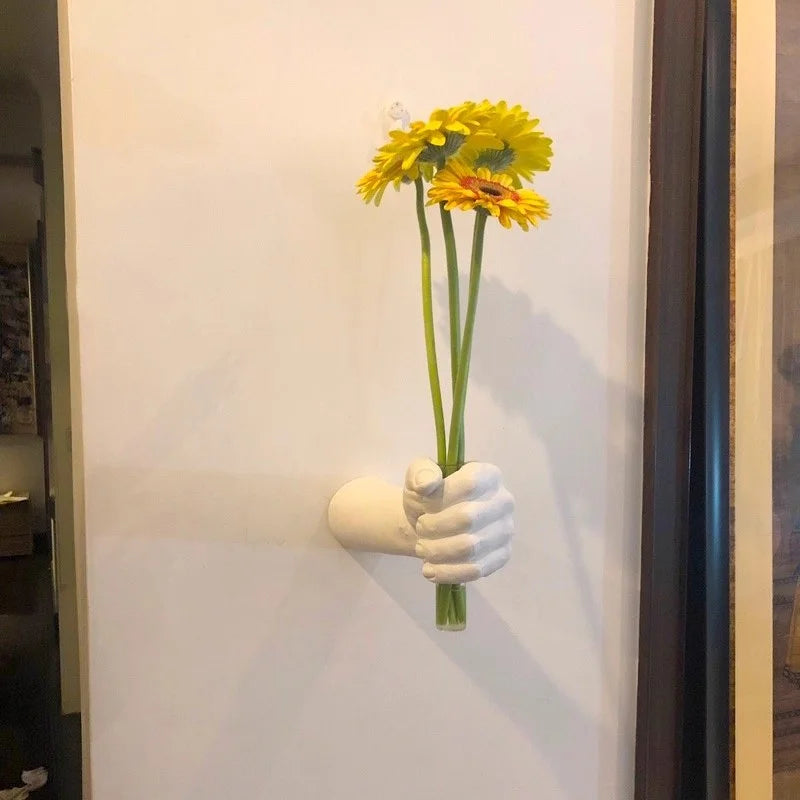 Fist-shaped wall vase holding yellow flowers in a small entryway or hallway