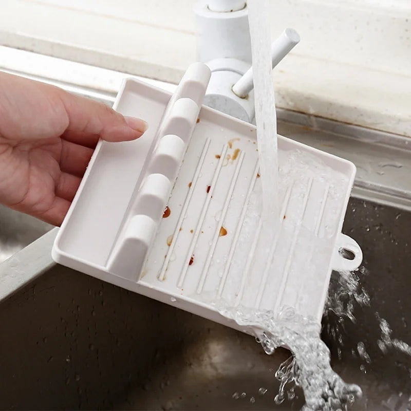 White kitchen utensil rest being rinsed under running water in a sink