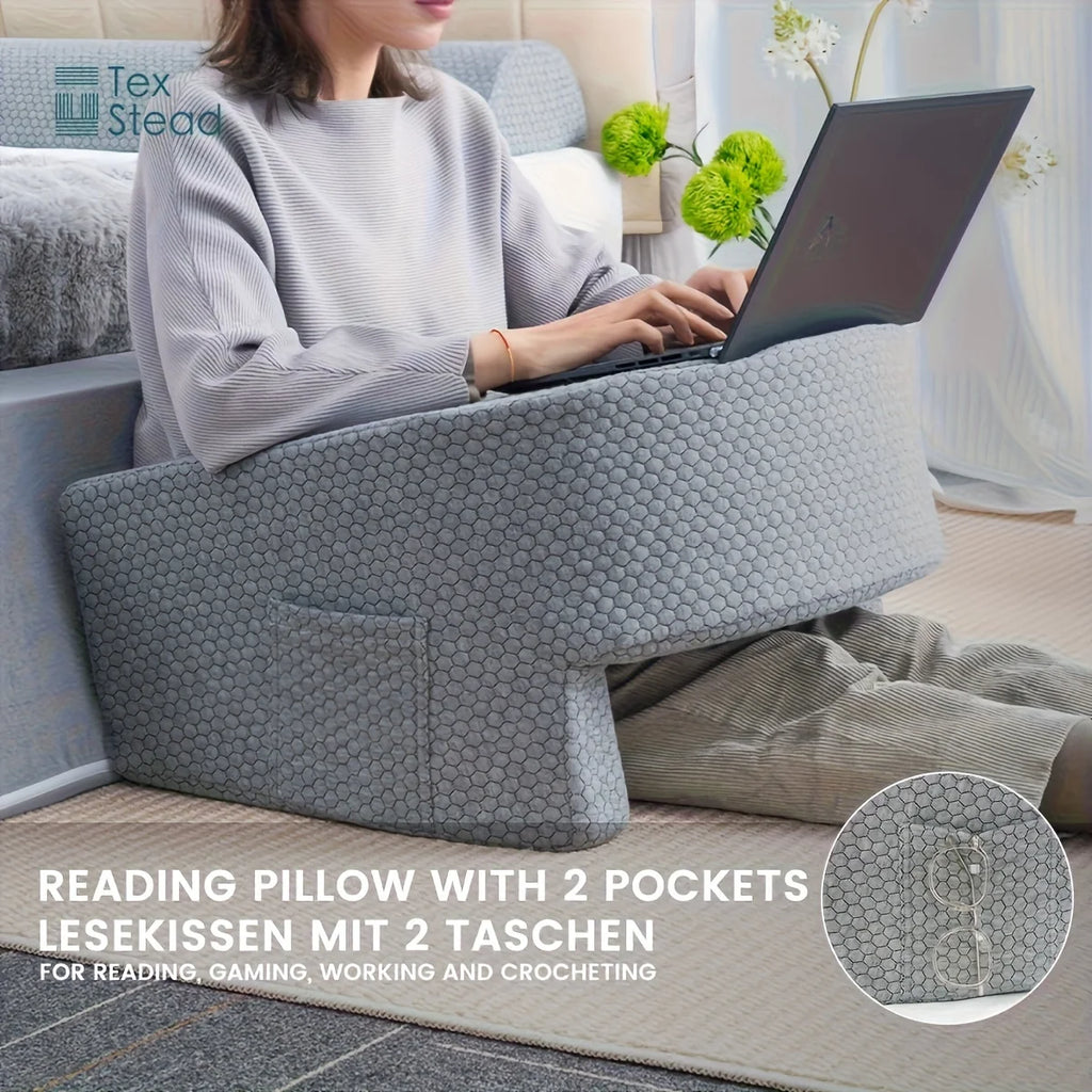 Person using extra large grey reading pillow with arm rests and side pocket while working on laptop in bed